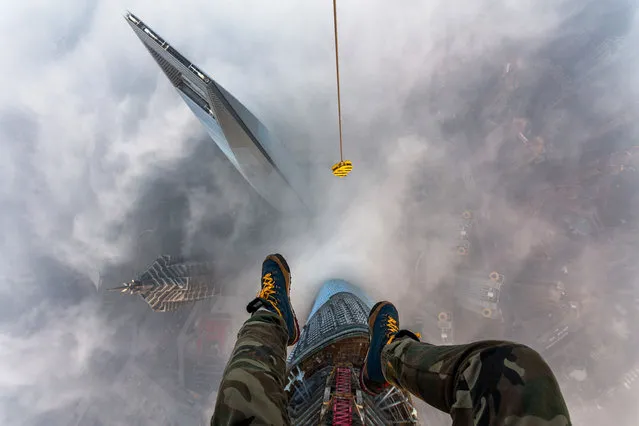 Vitaly Raskalov's feet dangle from the top of the Shanghai Tower, high above the Shanghai World Financial Centre. (Photo by Vitaly Raskalov/Caters News Agency)