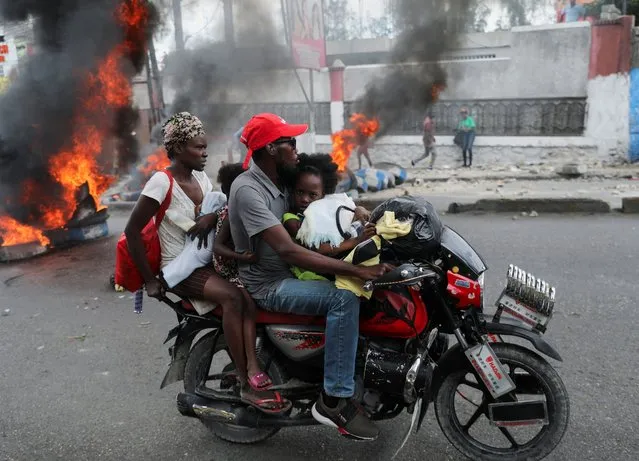 People on a motorcycle drive near a burning barricade set up in protest against the government, calling for the resignation of Prime Minister Ariel Henry, in Port-au-Prince, Haiti on February 5, 2024. (Photo by Ralph Tedy Erol/Reuters)