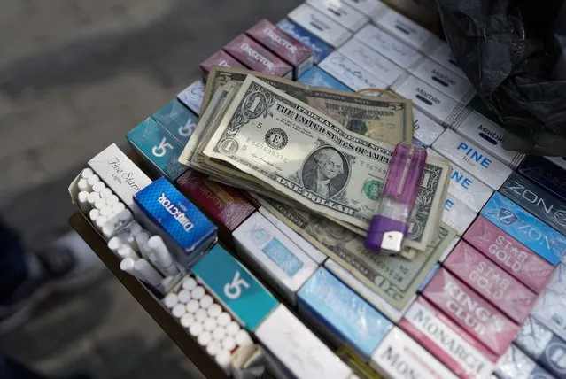 U.S. dollar bills, belonging to a street vendor, sit atop cigarettes for sale in Caracas, Venezuela, Friday, October 1, 2021. (Photo by Ariana Cubillos/AP Photo)