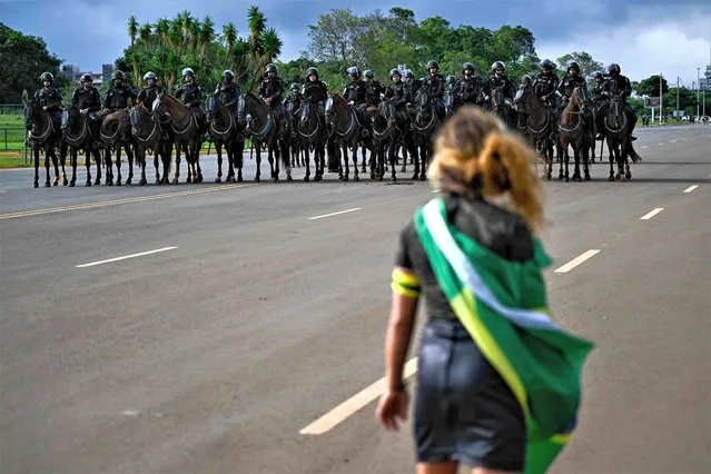 A demonstrator looks at mounted police forces while soldiers dismantle a camp by supporters of Brazil's far-right ex-president Jair Bolsonaro that had been set up in front of the Army headquarters in Brasilia, on January 9, 2023, a day after backers of the ex-president invaded the Congress, presidential palace and Supreme Court. (Photo by Mauro Pimentel/AFP Photo)