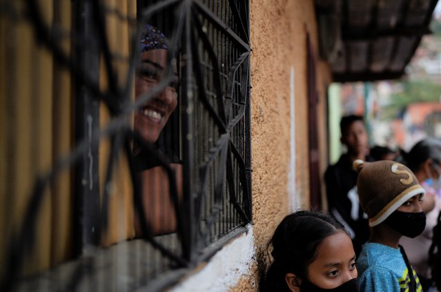 A woman smiles as she looks at a parade of mothers and children from soup kitchen through window, as they celebrate Christmas in the Antimano neighborhood of Caracas, Venezuela, Thursday, December 16, 2021. (Photo by Ariana Cubillos/AP Photo)