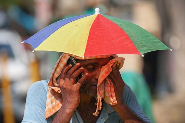 A vendor with an umbrella over his head talks on mobile phone as he wipes his face with a cloth on a hot summer day in Varanasi, India on May 27, 2024. (Photo by Niharika Kulkarni/AFP Photo)