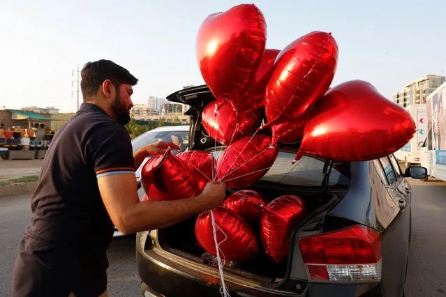 Mohammad Ali, 43, carries heart-shaped balloons on Valentine's Day, while putting them in a car trunk in Karachi, Pakistan, February 14, 2022. (Photo by Akhtar Soomro/Reuters)