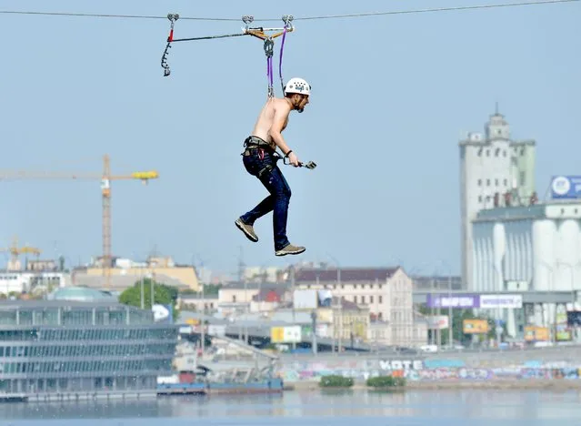 A man, hung by his back skin, crosses the Dniper river on a 552-meter long cable between the two banks of the river on May 23, 2014 in Kiev. (Photo by Sergei Supinsky/AFP Photo)