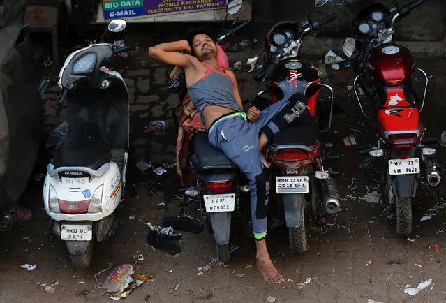 A man sleeps on a parked motorcycle outside a slum on a hot summer morning in Mumbai, India, May 25, 2017. (Photo by Danish Siddiqui/Reuters)
