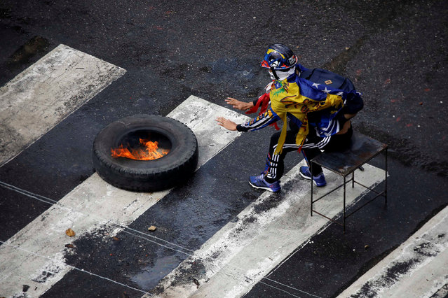 A demonstrators sits by a burning tire as clashes broke out with security forces while the Constituent Assembly election was being carried out in Caracas, Venezuela, July 30, 2017. (Photo by Carlos Garcia Rawlins/Reuters)