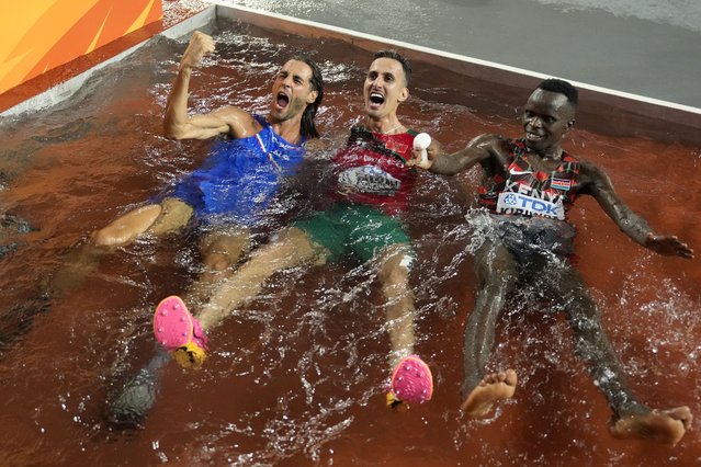 Gianmarco Tamberi, of Italy, left, Soufiane El Bakkali, of Morocco, center, and Abraham Kibiwot, of Kenya, celebrate in the steeplechase trap during the World Athletics Championships in Budapest, Hungary, Tuesday, August 22, 2023. Tamberi won the Men's high jump final, El Bakkali won the Men's 3000-meters steeplechase and Kibiwot finished third. (Photo by Ashley Landis/AP Photo)
