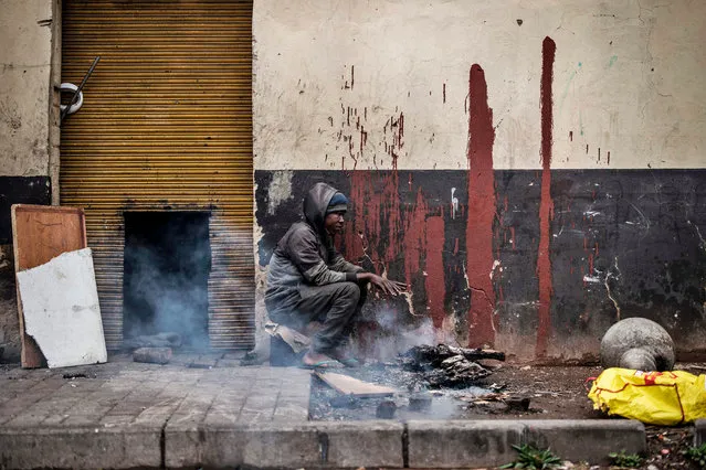 A homeless man warms up by burning wood in the CBD in Johannesburg, on April 28, 2020. (Photo by Marco Longari/AFP Photo)