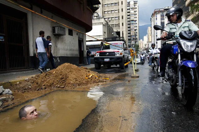 A worker is seen partially submerged under water as he tries to repair a broken pipe in Caracas, Venezuela, September 26, 2012. (Photo by Rodrigo Abd/AP Photo)