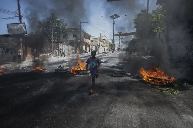 A young man walks past a burning barricade during a protest against fuel price hikes and to demand that Haitian Prime Minister Ariel Henry step down, in Port-au-Prince, Haiti, Thursday, September 15, 2022. (Photo by Joseph Odelyn/AP Photo)