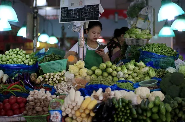 A vegetable vendor looks at her mobile phone at a market in Shanghai, China, September 10, 2015. China's manufacturers slashed prices at the fastest rate in six years in August as commodity prices fell and demand cooled, signalling stubborn deflation risks in the economy and adding to expectations for further stimulus measures. (Photo by Aly Song/Reuters)
