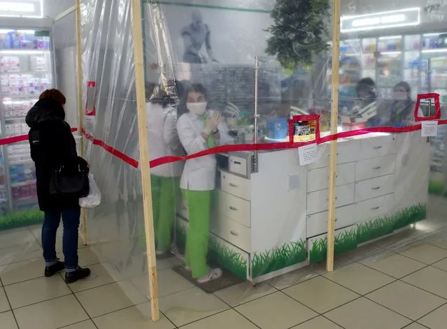 In this file photo taken on March 18, 2020 pharmacists wearing face masks are seen behind polyethylene membrane set around the counter in a pharmacy in the western Ukrainian city of Lviv. Ukraine has confirmed fourteen cases of COVID-19 and two death according to official figures published on March 18, 2020. (Photo by Yuri Dyachyshyn/AFP Photo)