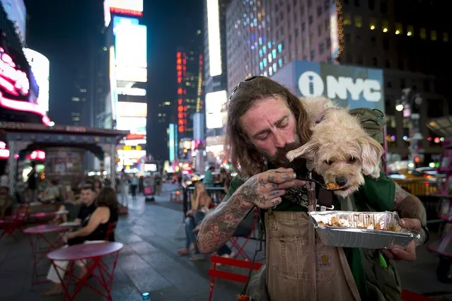 Deke Breuer feeds his dog Cahlupa some lasagna in Times Square in the Manhattan borough of New York, September 4, 2015. Breuer, originally from Detroit, have been living and traveling for the last few years and has taught his dog many tricks. (Photo by Carlo Allegri/Reuters)