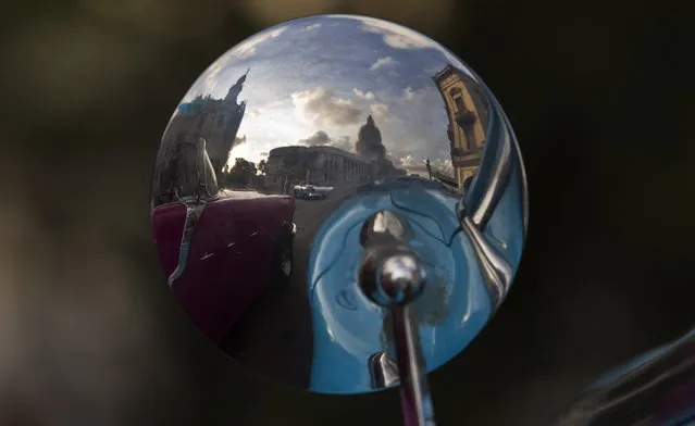 In this October 15, 2014 photo, American classic cars is reflected in a mirror in Havana, Cuba. The cars may gleam on the outside, but they're often battered, rolling monuments to ingenuity within. Many scavenge parts, particularly engines, from Soviet-era cars and trucks. (Photo by Franklin Reyes/AP Photo)