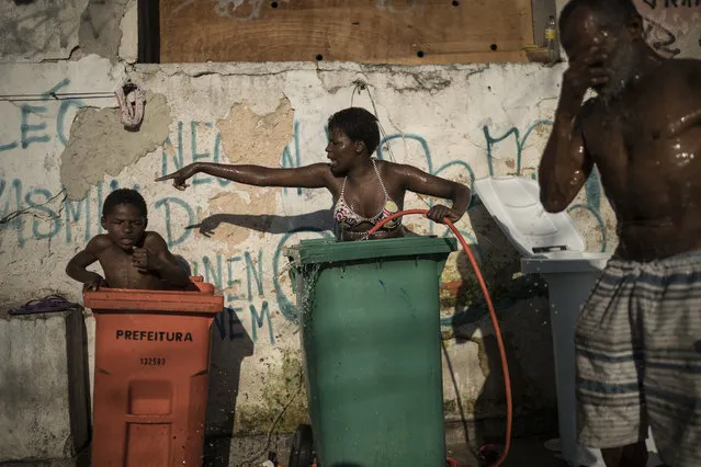 In this September 11, 2017 photo, a woman and youth use tall trash containers to shower outside their squatter building that used to house the Brazilian Institute of Geography and Statistics (IBGE) in the Mangueira slum of Rio de Janeiro, Brazil. The World Bank estimates that between the start of 2016 and the end of this year, 2.5 million to 3.6 million Brazilians will have fallen back below the poverty line of 140 Brazilian reais per month, about $44 at current exchange rates. (Photo by Felipe Dana/AP Photo)