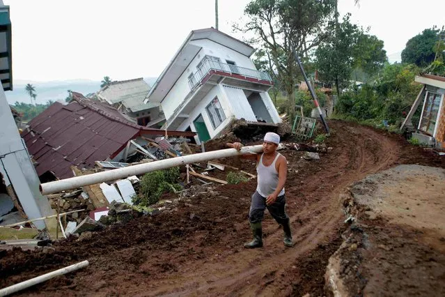 Opik Goparudin, 67, carries a duct near badly damaged houses after Monday's earthquake hit Cianjur, West Java province, Indonesia on November 25, 2022. (Photo by Ajeng Dinar Ulfiana/Reuters)
