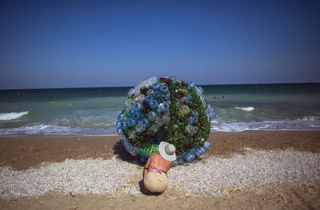 Tourists look at an art installation resembling the structure of the COVID-19 virus, made of plastic water bottles on the beach of the village Ezerets, Bulgaria, 23 August 2020. The art installation actually wants to show the pollution of plastic waste in the world's oceans. (Photo by Vassil Donev/EPA/EFE)