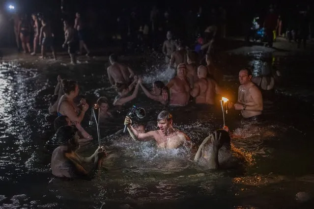 Lithuanian Orthodox believers bathe in the icy water shortly after midnight during a traditional Epiphany celebration in a lake near Vilnius, Lithuania, Thursday, January 19, 2023. Water that is blessed by a cleric on Epiphany is considered holy and pure until next year's celebration, and is believed to have special powers of protection and healing. (Photo by Mindaugas Kulbis/AP Photo)