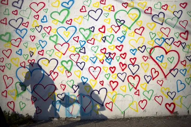 A couple casts shadows as they walk past a wall painted with hearts, an artwork created by Royal, on Wednesday, June 8, 2016, in Los Angeles. (Photo by Jae C. Hong/AP Photo)