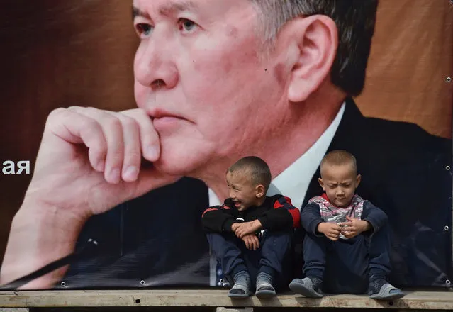 Boys sit on a bench under a campaign banner for the Social Democratic Party of Kyrgyzstan featuring an image of former Kyrgyz president Almazbek Atambayev in the village of Arashan, some 20km from Bishkek, on September 30, 2020. Kyrgyzstan will hold parliamentary election on October 4, 2020. (Photo by Vyacheslav Oseledko/AFP Photo)