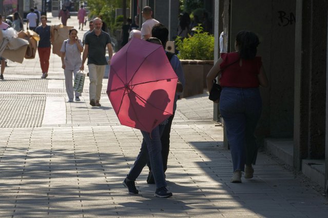 A woman walks with an umbrella to protect against the sun in Madrid, Spain, Wednesday, July 13, 2022. Weather forecasters say Spain is expected to have its second heat wave in less than a month and that it will last at least until the weekend. Meteorologists said an overheated mass of air and warm African winds are driving temperatures in the Iberian Peninsula beyond their usual highs. (Photo by Paul White/AP Photo)