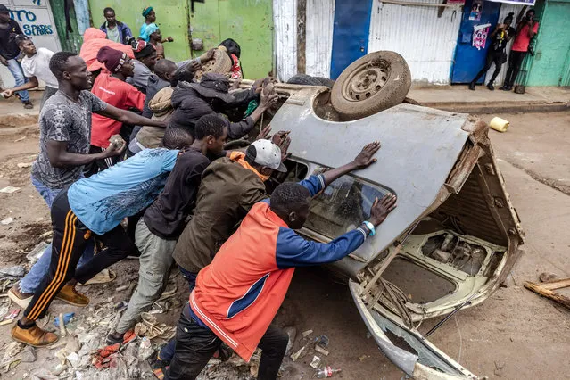 Opposition supporters push a car they use as a barricade during clashes with Kenya Police Officers in Nairobi, Kenya on March 27, 2023. (Photo by Luis Tato/AFP Photo)