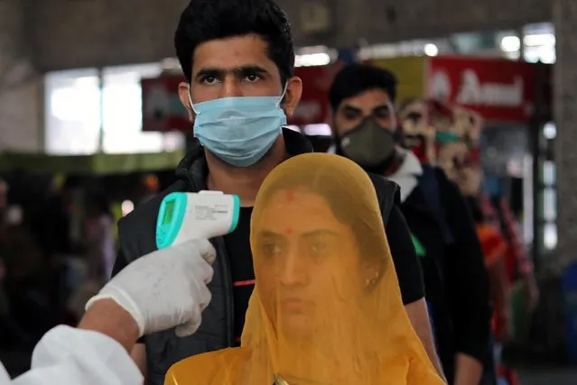 A health worker in personal protective equipment (PPE) checks the temperature of passengers amid the spread of the coronavirus disease (COVID-19), at a railway station in Mumbai, India, December 19, 2020. India's coronavirus cases have crossed 10 million with new infections dipping to their lowest levels in three months, as the country prepares for a massive COVID-19 vaccination in the new year. (Photo by Francis Mascarenhas/Reuters)