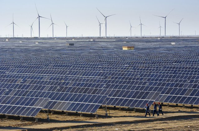 Workers walk past solar panels and wind turbines (rear) at a newly-built power plant in Hami, Xinjiang Uighur Autonomous Region, China, September 17, 2015. China's power consumption in August rose 1.9 percent from a year earlier to 512.4 billion kilowatt-hours (kWh), figures from the country's National Energy Administration (NEA) showed on Tuesday. (Photo by Reuters/Stringer)