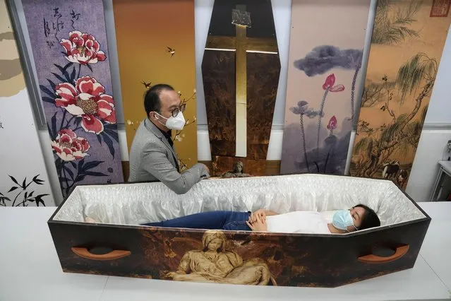 Wilson Tong, CEO of LifeArt Asia, left, talks to a reporter who tries out a catholic-designed paper coffin at Tong's factory in Hong Kong, Friday, March 18, 2022. Hong Kong is running short of coffins during its deadliest outbreak of the coronavirus pandemic, which has cost about 6,000 lives so far this year.  LifeArt, a company in Hong Kong is trying to make an alternative, cardboard coffin, which it says is environmentally-friendly. (Photo by Kin Cheung/AP Photo)
