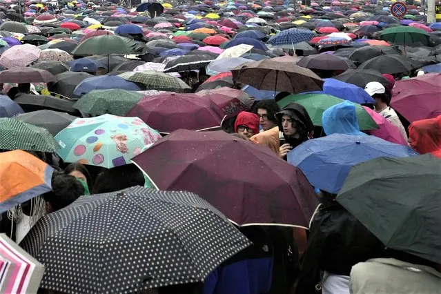 People take shelter from the rain during a free concert organized by the main Italian Labour Unions on May Day in St. John in Lateran Square in Rome, Monday, May 1, 2023. (Photo by Alessandra Tarantino/AP Photo)
