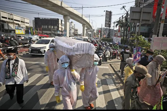 Government officials in protective suits carry a mock coffin as they walk around a busy intersection during a coronavirus awareness campaign to remind people of the risk of contracting COVID-19 and to always obey health protocols to curb the spread of the outbreak in Jakarta, Indonesia, Friday, August 28, 2020. (Photo by Dita Alangkara/AP Photo)