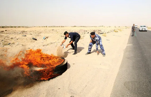 Iraqi policemen throw sand to put out a fire set by protesters, during a protest at the main entrance to the giant Zubair oilfield near Basra, July 17, 2018. The protests that have gripped Iraq are the result of years of social anger that had been swept under the carpet as the country battled the Islamic State group, experts say. (Photo by Essam al-Sudani/Reuters)