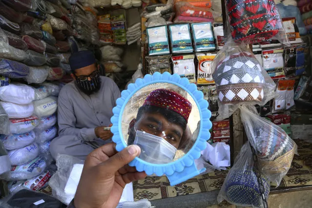 A man tries on a traditional cap in preparation for the upcoming Muslim fasting month of Ramadan, in Peshawar, Pakistan, Thursday, April 8, 2021. Muslims usually increase their religious activities during Ramadan, which begins with the new moon probably next week. Muslims around the world are trying to work out how to maintain the many cherished rituals of Islam's holiest month amid the COVID-19 coronavirus pandemic. (Photo by Muhammad Sajjad/AP Photo)