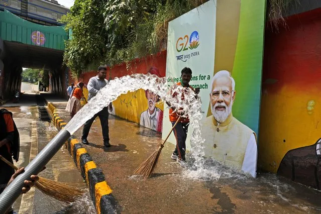 Municipal workers wash a side walk near a billboard featuring Indian Prime Minister Narendra Modi ahead of this week's summit of the Group of 20 nations, in New Delhi, India, Thursday, September 7, 2023. (Photo by Manish Swarup/AP Photo)