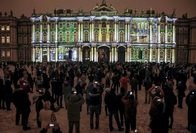 People watch and take pictures of illuminated Hermitage State Museum during a light show marking the Day of Hermitage at the Dvortsovaya (Palace) square in St. Petersburg, Russia, Wednesday, December 7, 2016. (Photo by Dmitri Lovetsky/AP Photo)