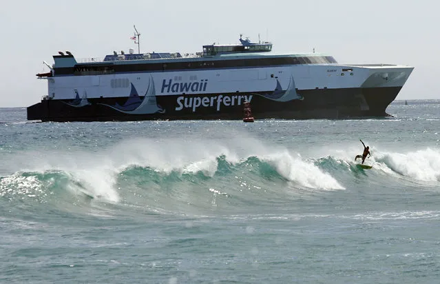 In this June 30, 2007, file photo, a surfer catches a wave at Kakaako Waterfront Park as the Hawaii Superferry approaches Aloha Towers in Honolulu. Hawaii officials are exploring what it would take to run a ferry between islands. But they're facing skepticism over costs and whether there's a ferry system residents would accept. But the idea is bringing back memories of the Superferry, an emotional and expensive failure in Hawaii history. Years ago protesters blocked the Superferry from docking in Kauai. And a court later ordered the ferry to stop running because the state didn't do a proper environmental review. (Photo by Marco Garcia/AP Photo)