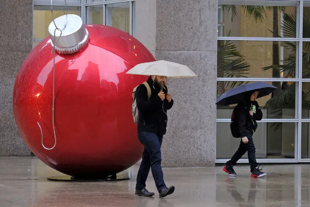 A man and a woman walk in the rain past a holiday ornament Thursday, November 29, 2018, in San Francisco. A storm moving into California on Thursday brought rain that threatened to unleash debris flows in wildfire burn areas and snow that could cause travel problems in the Sierra Nevada. (Photo by Eric Risberg/AP Photo)