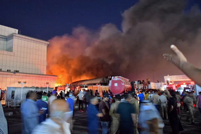 People gather as a massive fire engulfs the coronavirus isolation ward of Al-Hussein hospital in the southern Iraqi city of Nasiriyah, late on July 12, 2021. (Photo by Asaad Niazi/AFP Photo)
