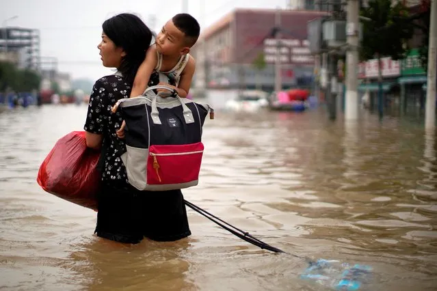 A woman carrying a child and belongings wades through floodwaters following heavy rainfall in Zhengzhou, Henan province, China on July 23, 2021. (Photo by Aly Song/Reuters)