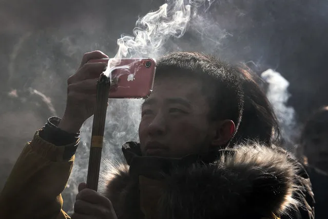 In this Tuesday, January 1, 2019, photo, a Chinese man uses iPhone to take picture as he prays for health and fortune on the first day of the New Year at Yonghegong Lama Temple in Beijing. Apple acknowledged that demand for iPhones is sagging, a warning likely to roil financial markets. It confirmed investor fears that the company's most profitable product has lost some of its luster. CEO Tim Cook said that iPhone sales fell well below projections, especially in China, amid a trans-Pacific trade war and concern over global economic weakness. (Photo by Andy Wong/AP Photo)