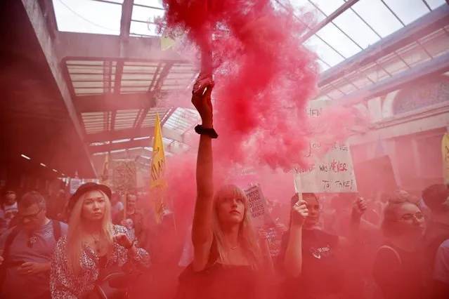 A climate activist from the Extinction Rebellion lets off a smoke bomb at a gathering for a National Animal Rights March at Smithfield Market in London on August 28, 2021 during the group's “Impossible Rebellion” series of actions. Climate change demonstrators from environmental activist group Extinction Rebellion continued with their latest round of protests in central London, promising two weeks of disruption. (Photo by Tolga Akmen/AFP Photo)