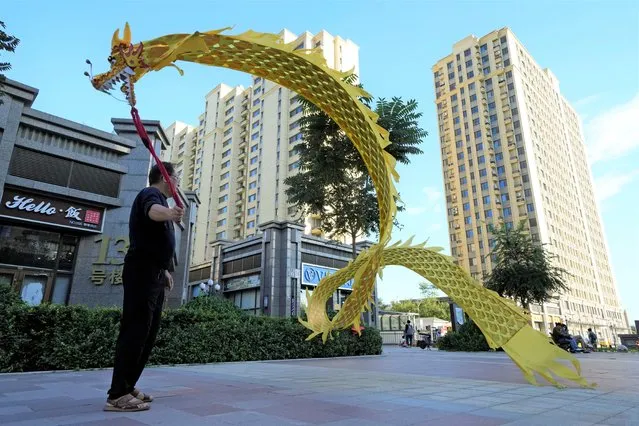 A resident wields a cloth dragon outside the Evergrande Yujing Bay residential complex in Beijing, China, Tuesday, September 21, 2021. Global investors are watching nervously as one of China's biggest real estate developers struggles to avoid defaulting on tens of billions of dollars of debt, fueling fears of possible wider shock waves for the financial system. (Photo by Ng Han Guan/AP Photo)