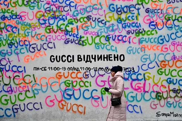 A woman walks past the Gucci fashion house shop window covered with protective chipboard against fragments of shelling with a sign reading, “Gucci is open”, in the center of Ukrainian capital of Kyiv on December 12, 2022. (Photo by Sergei Supinsky/AFP Photo)