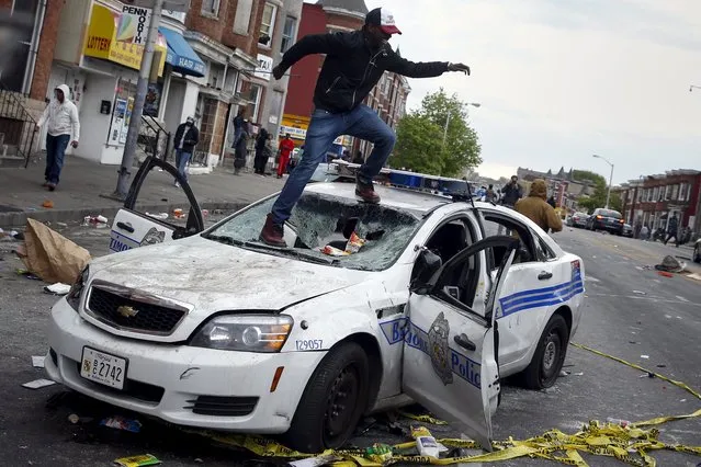 Demonstrators jump on a damaged Baltimore police department vehicle during clashes in Baltimore, Maryland April 27, 2015. Maryland Governor Larry Hogan declared a state of emergency and activated the National Guard to address the violence in Baltimore, his office said on Monday. (Photo by Shannon Stapleton/Reuters)