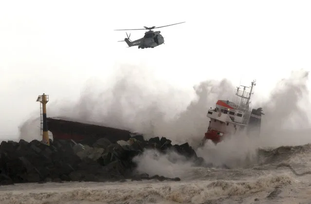 A military helicopter flies over a Spanish cargo ship that slammed into a jetty in choppy Atlantic Ocean waters off Anglet, southwestern France, Wednesday, February 5, 2014. The ship had been heading to a nearby port to load up with cargo when its engine failed and the rough waves carried it into the jetty. (Photo by Bob Edme/AP Photo)