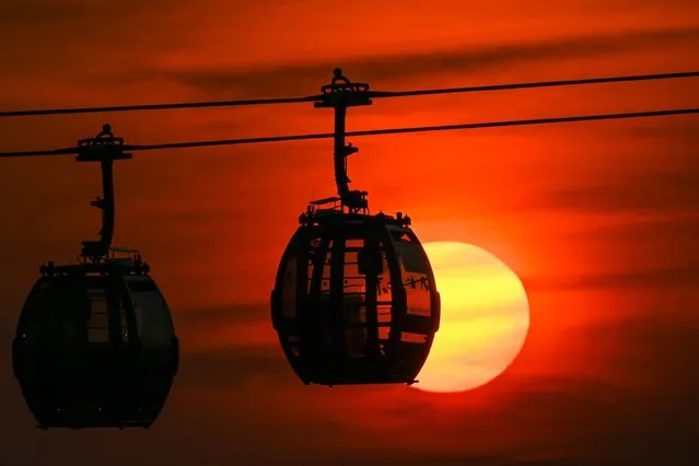 The sun sets behind cable car cabins in Singapore on October 15, 2021. (Photo by Roslan Rahman/AFP Photo)
