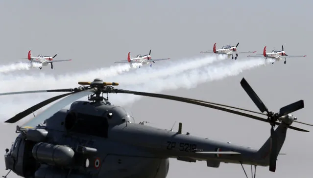 The Yakovlevs, a UK based aerobatic team flying Russian designed Yakovlev aircrafts, fly over an Indian Air Force helicopter on the third day of Aero India 2017 at Yelahanka air base in Bangalore, India, Thursday, February 16, 2017. Aero India is a biennial event with flying demonstrations by stunt teams and militaries and commercial pavilions where aviation companies display their products and technology. (Photo by Aijaz Rahi/AP Photo)