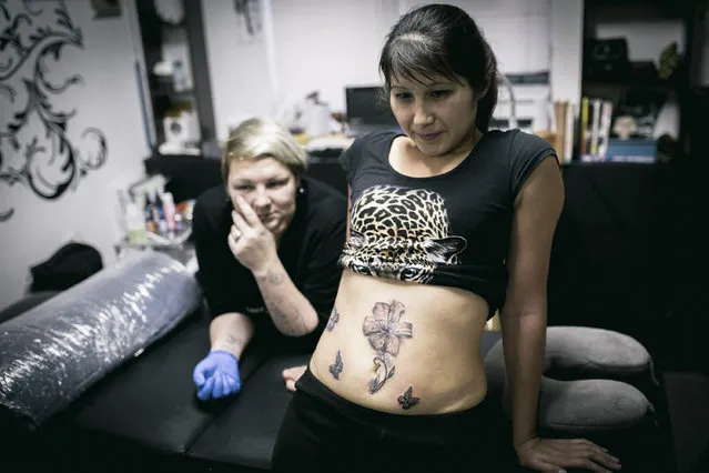 In this photo taken on Tuesday, December 6, 2016 Lyaysan, right, and tattoo artist Yevgeniya Zakhar look in the mirror at the tattoo Lyaysan had done to conceal a scar from a domestic violence attack, in Ufa, Russia. Yevgeniya Zakhar, a Russian tattoo artist from Ufa, a city about 1,200 kilometers (745 miles) east of Moscow, gives free tattoos to victims of domestic abuse, to cover their scars. (Photo by Vadim Braydov/AP Photo)