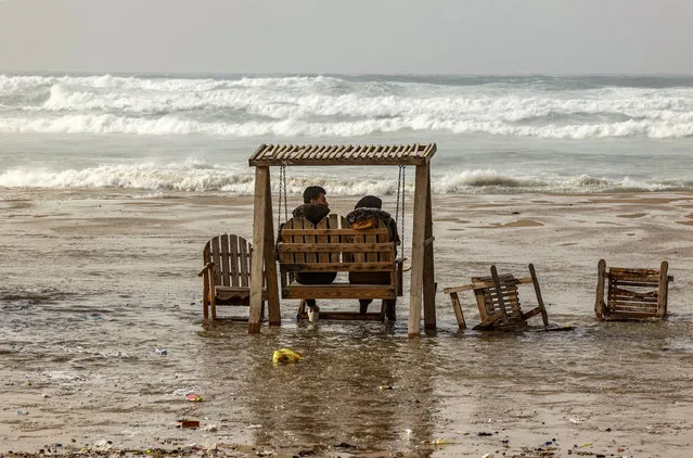 A couple sits on a swing during stormy weather along a beach by the Mediterranean Sea in Gaza City on December 8, 2021. (Photo by Mahmud Hams/AFP Photo)
