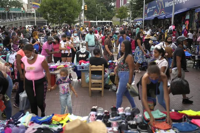 People shop at an outdoor market in Caracas, Venezuela, Friday, November 26, 2021. At malls and few stores, Venezuelans are taking the opportunity to buy clothes and other articles with generous Black Friday discounts. (Photo by Ariana Cubillos/AP Photo)